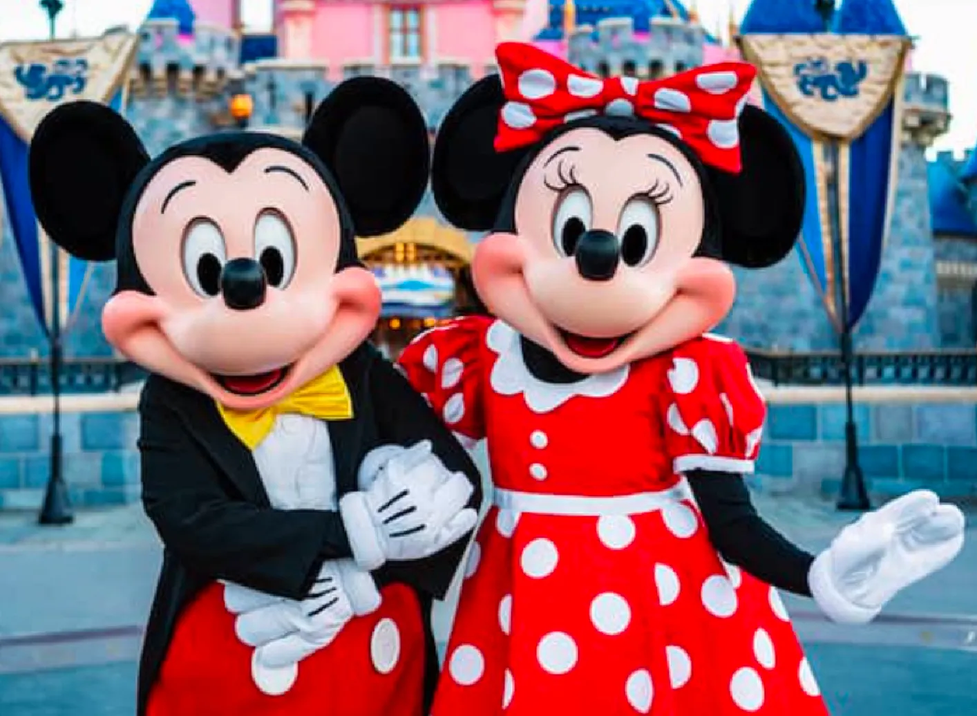 Mickey and Minnie Mouse standing together in front of park rides